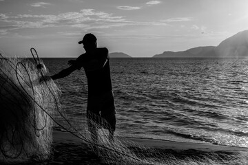 Greyscale shot of a man's silhouette with a fishing net in the lake in Brazil