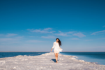 Fototapeta na wymiar A beautiful woman walks along the seashore in a beach dress.
