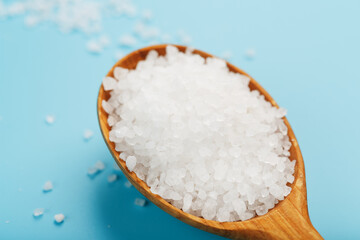 Large sea salt crystals in a wooden spoon with greens on a blue background. Universal spice, free space
