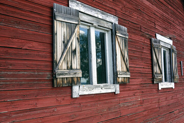 Old red timber wall with two windows. Charming rustic house with idyllic shutters.