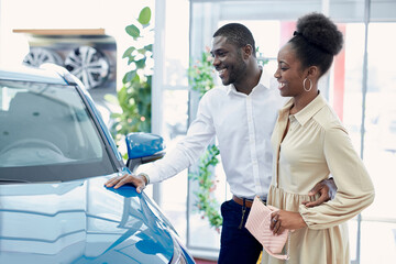 Fototapeta premium young african married couple in the search of the best car in dealership, they have conversation, discuss automobiles