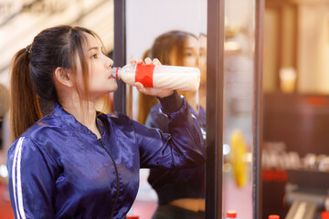 Young asian woman drinking protein shake from bottle after workout exercise for muscle at fitness...