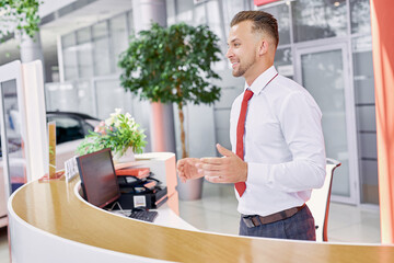 pleasant caucasian salesman welcomes customers in dealership, man is glad to see clients