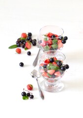 Salad of fresh berries and greens, strawberries, black currant and spinach in a glass on a white background