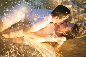 wet lovers lie on beach in water and kiss. 