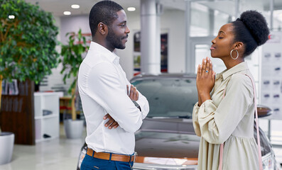 side view on good-looking cute african female begging her husband in car showroom, woman want to get new auto
