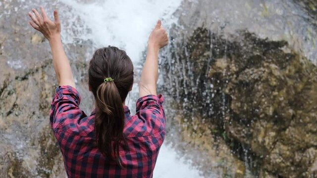 Young woman touching water hands from waterfall drops. People travel enjoying nature and life concept. Slow video