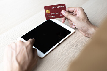 Asian man is holding a credit card and paying with a tablet.