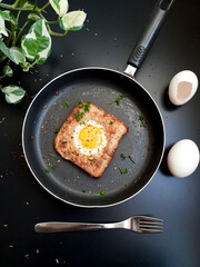 Egg in a hole topped with chili flakes, oregano, and herbs on a pan.