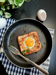 Egg in a hole topped with chili flakes, oregano, and herbs on a pan.