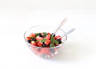 Salad of fresh berries and greens, strawberries, black currant and spinach in a glass bowl on a white background