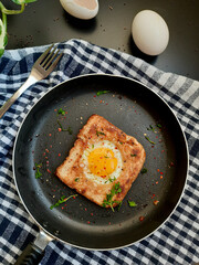 Egg in a hole topped with chili flakes, oregano, and herbs on a pan.