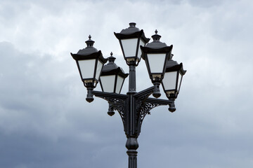 Beautiful cast iron vintage street lamp on a background of blue sky and clouds