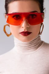 Portrait of beautiful woman in red sunglasses looking at camera isolated on grey © LIGHTFIELD STUDIOS