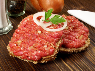 Spicy Beef Tartar Meat on a Bread Roll with Onions on wooden Background
