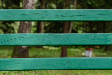 Obraz premium A view of the garden through a green wooden picket fence, nailed horizontally with wide gaps, with trees and green grass in the background.