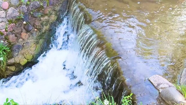 Beautiful sunny waterfall of a mountain river. Old stone bridge with seething water