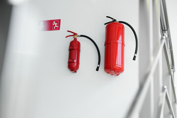 Fire extinguishers and emergency exit sign on white wall indoors