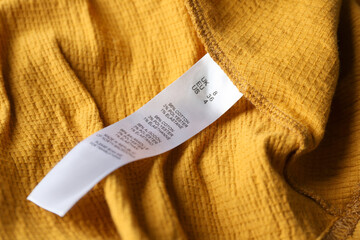 Clothing label with size and content information on yellow garment, closeup