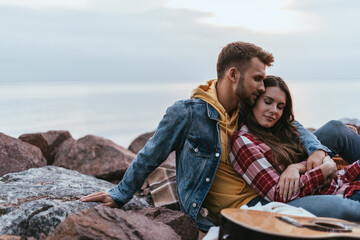 selective focus of handsome man hugging girlfriend near acoustic guitar