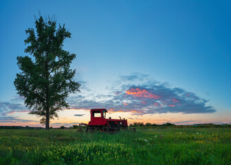 Beautiful sunset over field and old rusty tractor