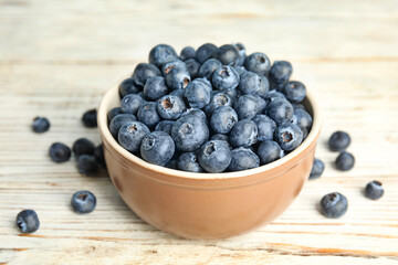 Tasty ripe blueberries in bowl on white wooden table