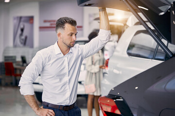handsome caucasian businessman is examining a car before buying it, he checks all characteristics and features of auto