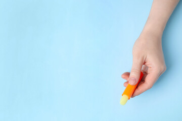 Woman holding hygienic lipstick on light blue background, top view. Space for text