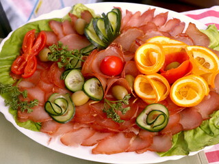 Homemade dried prosciutto with cherries, peppers, cucumbers and olives on white plate