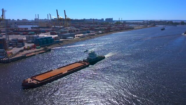 Aerial view of a row of construction or cargo cranes on the river bank with a barge passing by. Ship docks off Kanonersky Island. Industrial port with water barges and transport tugs.