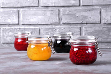Jams assortment in glass jars against the grey brick wall. Strawberry, orange, bilberry and raspberry jams