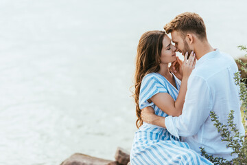 happy woman touching face of handsome boyfriend near river