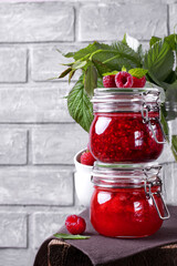 Raspberry and strawberry jam in glass jars against the grey background