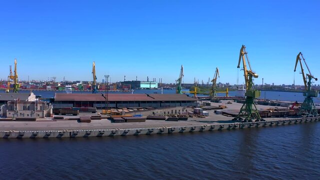 Aerial view of a row of construction or cargo cranes on the river bank. Ship docks off Kanonersky Island. Industrial port with water barges and transport tugs.