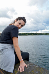 Fototapeta na wymiar Girl sitting on a wall, enjoying the fresh air, in front of a lake in Edgbaston, Birmingham, Uk.