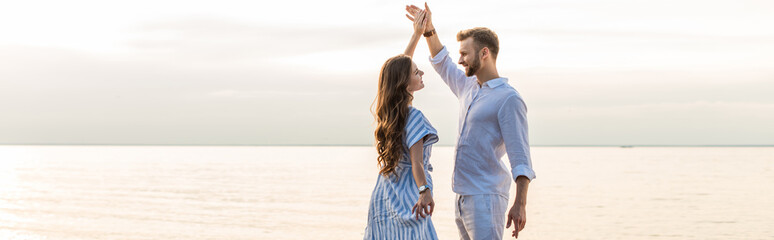 panoramic shot of happy couple holding hands and dancing near lake