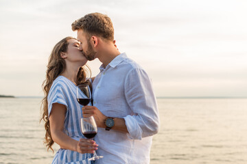 Fototapeta na wymiar couple kissing and holding glasses with red wine near lake