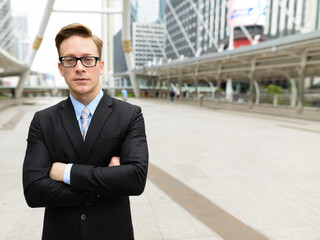 Young handsome blond businessman with arms crossed in the city outdoors