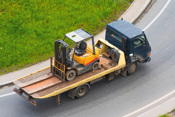 A truck is transporting loader forklift on the road.