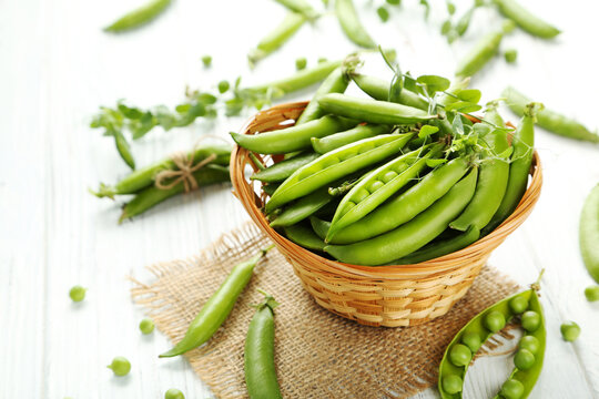 Green pea pods in basket on white wooden table