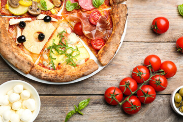 Slices of different pizzas on wooden table, flat lay