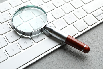 Magnifier glass and keyboard on light grey stone background, closeup. Find keywords concept