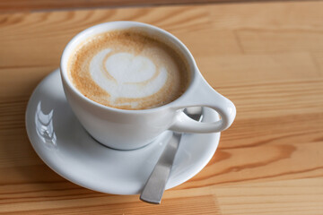 A white cup of coffee with heart pattern on wooden table