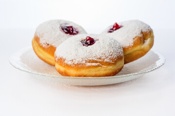 Obraz na płótnie Canvas Three donuts on a glass plate on a white background decorated with sugar powder and strawberry jam