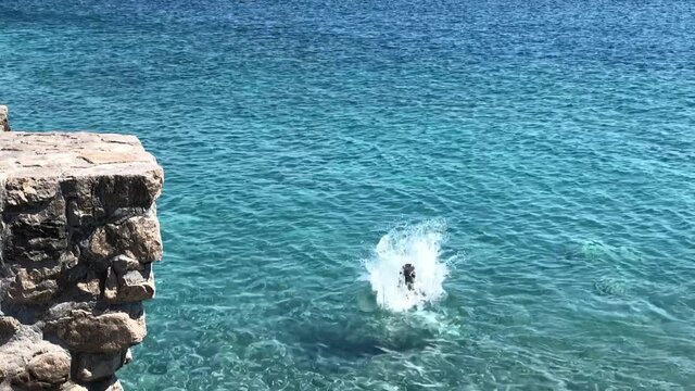 Brave girl jumping off a cliff into the sea in slow motion