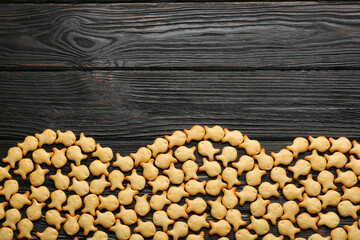 Delicious goldfish crackers on black wooden table, flat lay. Space for text