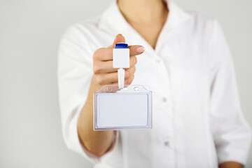 Female hand showing blank white bagde on grey background