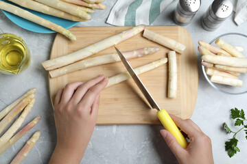 Woman cutting fresh white asparagus at grey marble table, top view
