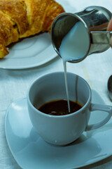 still life con taza de cafe con medialuna y jarra con leche sobre mantel blanco