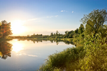 Summer background - calm river among birch groves, sunset over the river. Summer landscape, water surface.